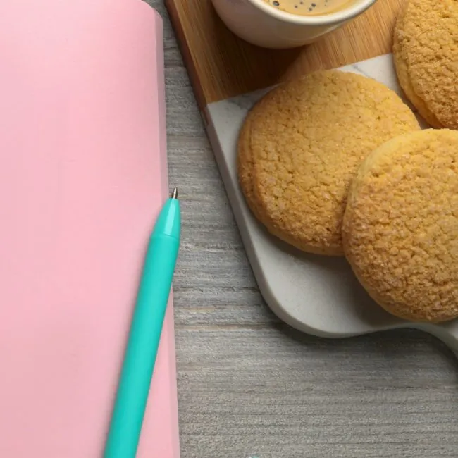 Notebook on a table with muffins, pen and coffee