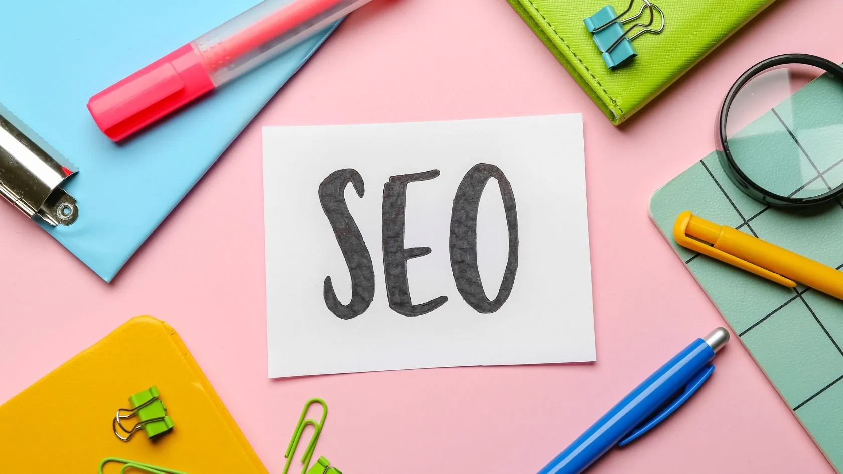 Pens and Sticky Notes on a pink desk with SEO paper in the middle